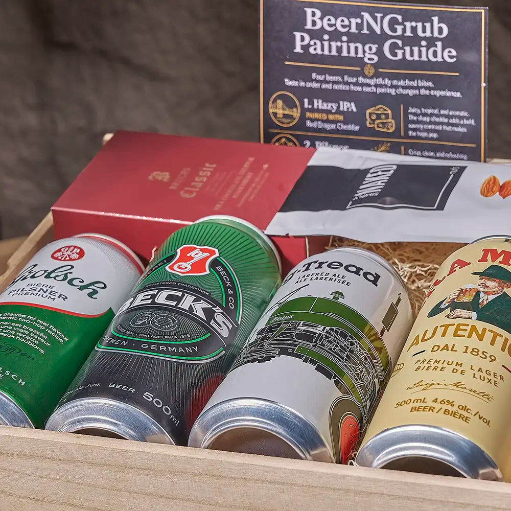 A curated beer pairing gift box containing four different beer cans, a red and gold Clasici box, a white and black MUGEN bag, and a 'BeerNGrub Pairing Guide' booklet, arranged in a wooden tray.