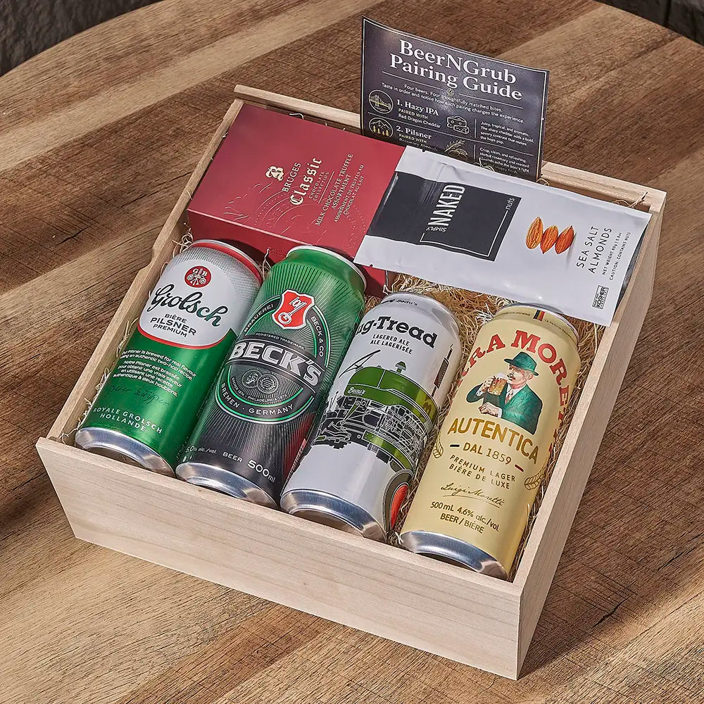 A wooden gift box filled with assorted beer cans, a red book, a black-and-white booklet, and a standing card titled 'BeerNGrub Pairing Guide,' arranged on a wooden table.