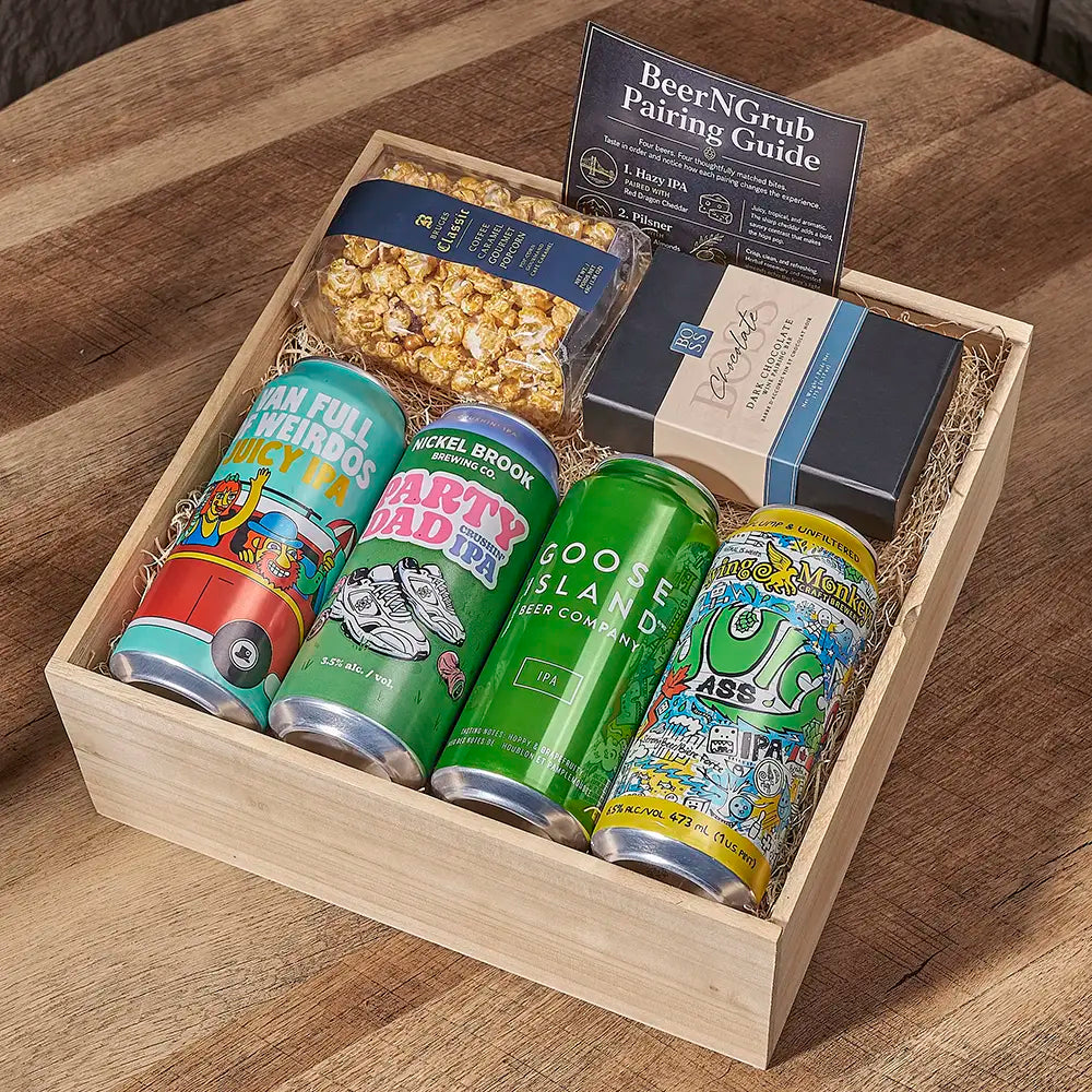 A wooden gift box filled with four craft beer cans, a bag of popcorn, a small box, and a BeerNGrub pairing guide, arranged on a wooden table.