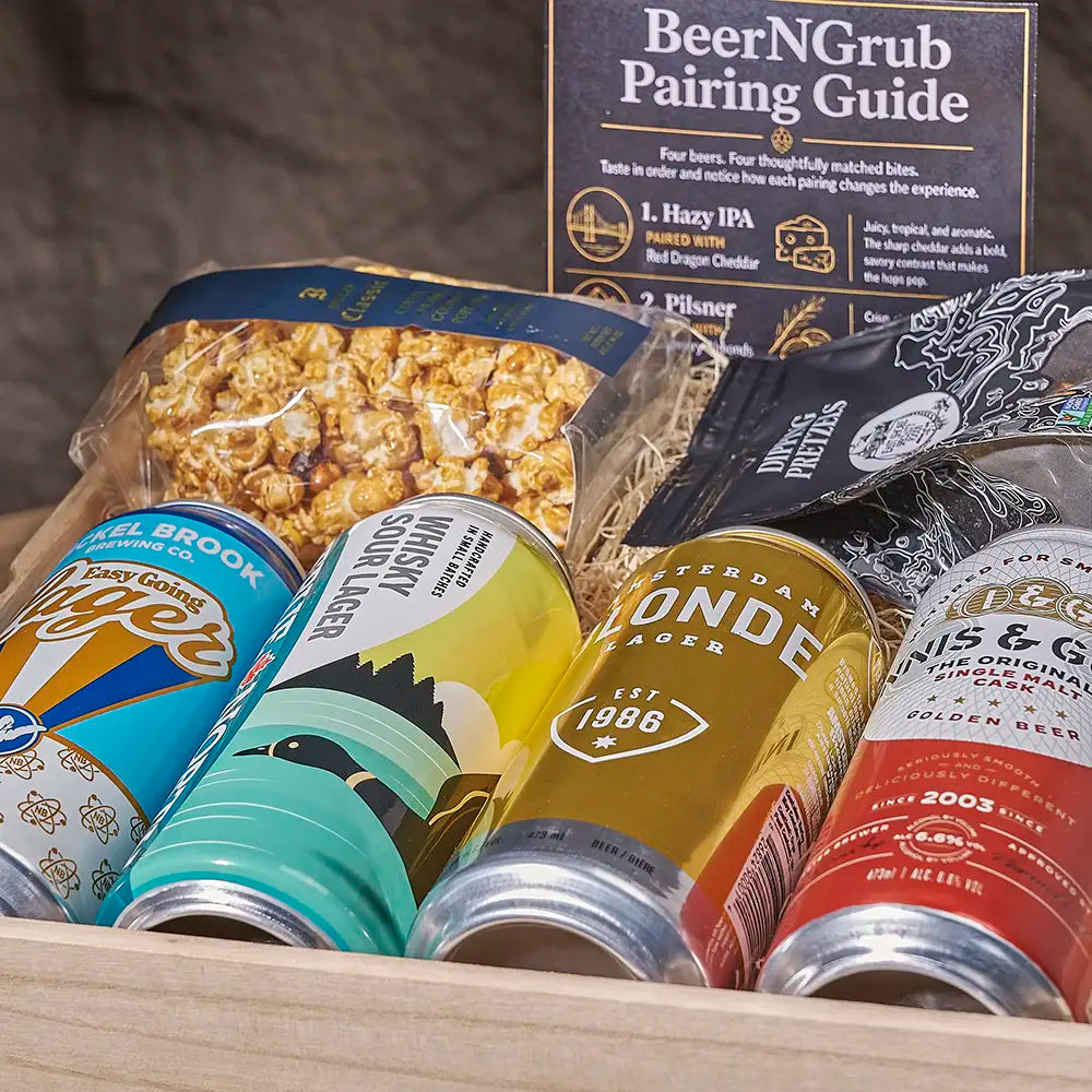 A curated beer and snack gift box featuring a 'BeerNGrub Pairing Guide' booklet, a bag of popcorn, a bag of pretzels, and four assorted craft beer cans in the foreground.