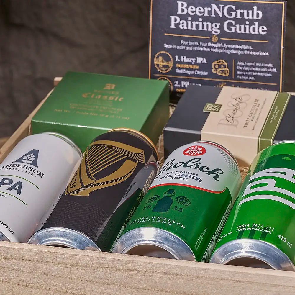 A curated selection of beer cans arranged in a wooden tray with a 'BeerNGrub Pairing Guide' card behind them. Visible cans include Anderson Stout Ales IPA, a black-and-gold harp-patterned beer, a green Bielsen Lager, and a green India Pale Ale.