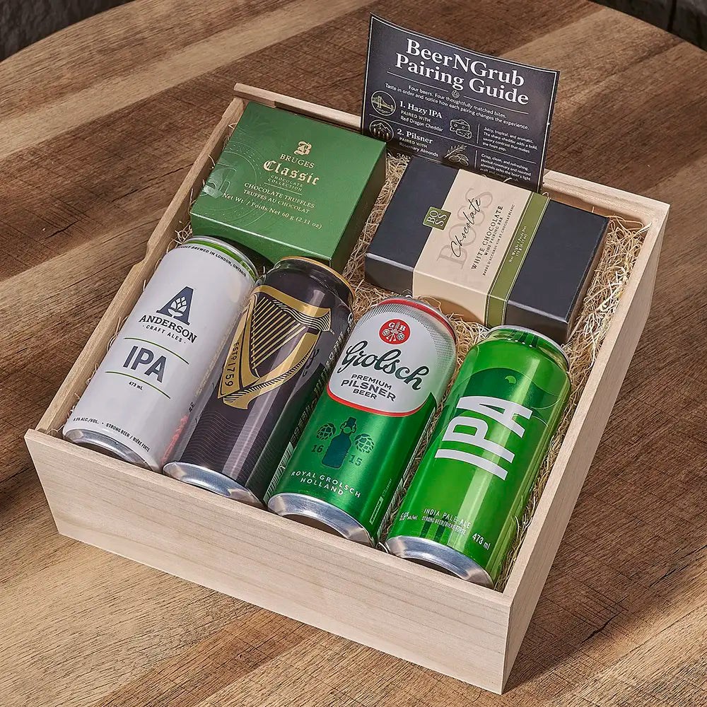 A wooden gift box filled with four beer cans, a green bottle, and a pairing guide booklet, arranged on a wooden table.