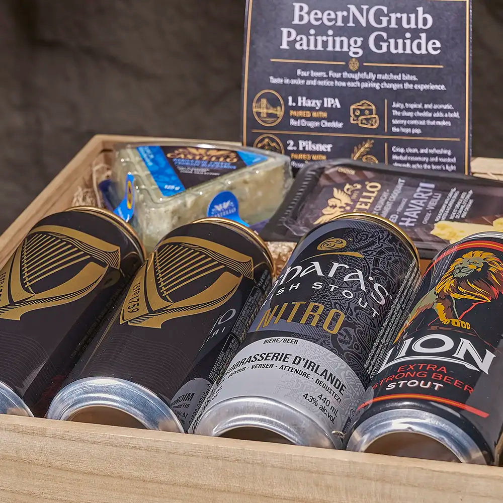 A curated beer and cheese pairing gift set arranged in a wooden box, featuring a 'BeerNGrub Pairing Guide' booklet, a block of cheese, and several stout and IPA beer cans including Parasol Stout and Lion Extraordinary Stout.