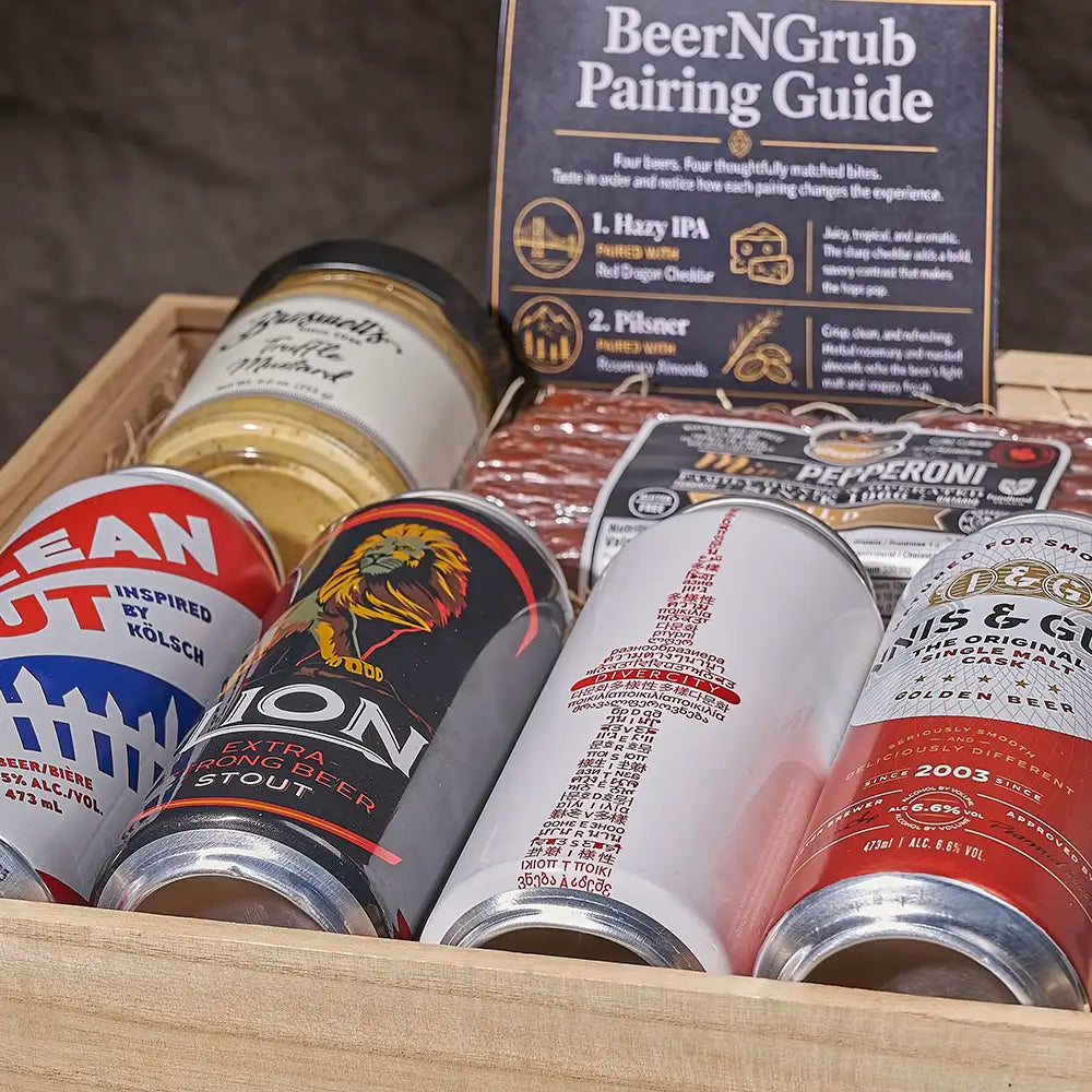 A wooden gift box filled with assorted beer cans and a printed pairing guide titled "BeerNGrub Pairing Guide." Visible products include a blue-and-white can, a black-and-gold can with a lion graphic, a white can with red text, and a red-and-white can, alongside packaged snacks and a guide card.