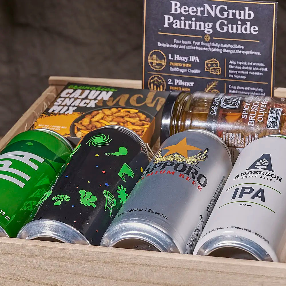 A curated beer and snack gift box containing four different craft beer cans, a Cajun Snack Mix bag, and a BeerNGrub pairing guide, arranged inside a wooden crate.