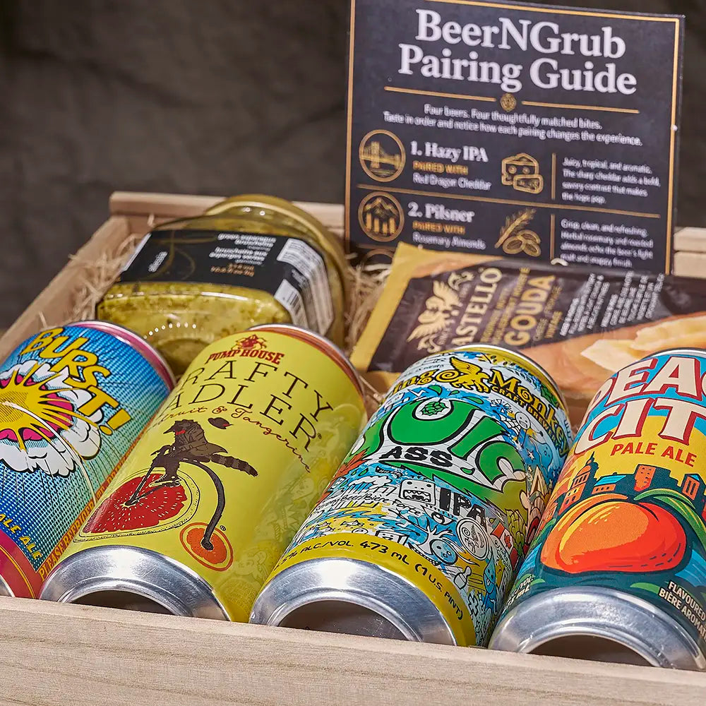 A curated beer pairing gift box filled with colorful canned ales, a jar of pickled ginger, a cheese wedge, and a BeerNGrub pairing guide card in a wooden tray.