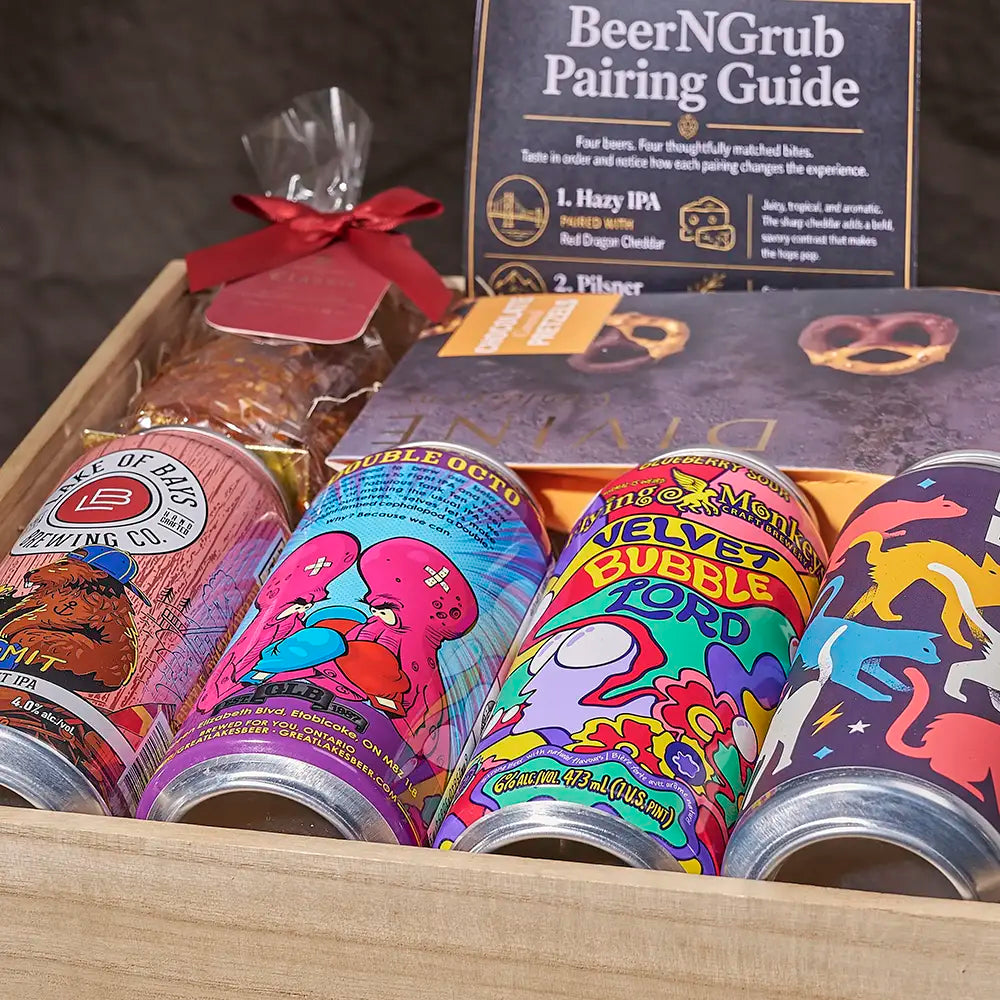 A curated beer gift box set displayed in a wooden tray, featuring four colorful craft beer cans, a bag of pretzels tied with a red ribbon, a 'BeerNGrub Pairing Guide' card, and a dark beer box. The cans have vibrant, cartoonish illustrations including a pink octopus, a purple creature, and a blue dinosaur.