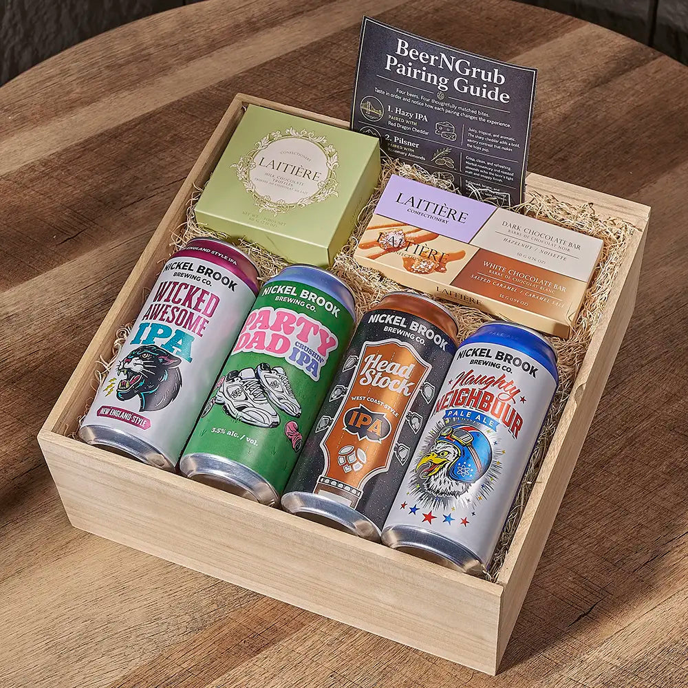 A wooden gift box filled with four craft beer cans, a green Lattiere box, a pairing guide card, and shredded paper on a wooden table. The cans are from Nickel Brook and Pappy Van Winkle's.