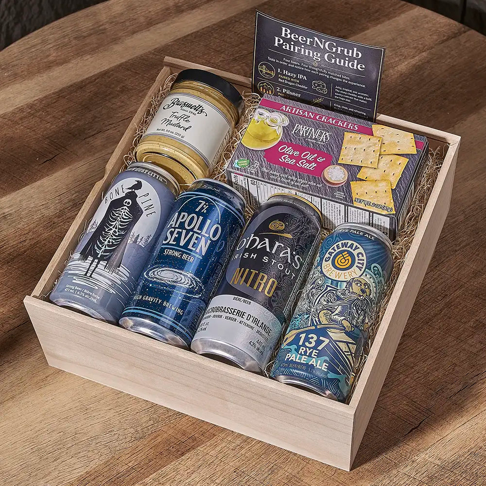 A wooden gift box filled with beer cans, a jar, crackers, and a painting guide, photographed on a wooden table. Visible brands include The Apollo Seven, Maris, and 137 Ales.