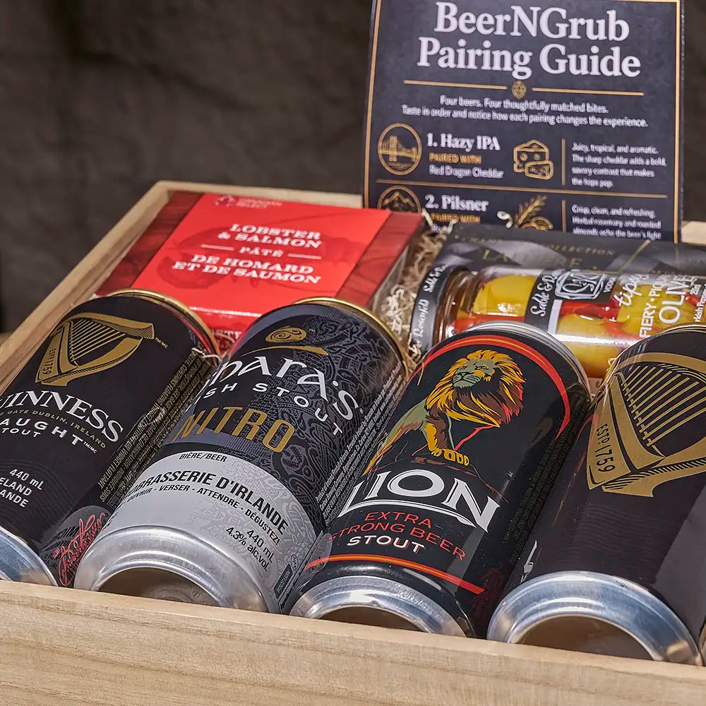 A wooden gift box filled with assorted beer-related items, including multiple stout cans, a red lobster salmon package, and a BeerNGrub pairing guide card standing behind them.